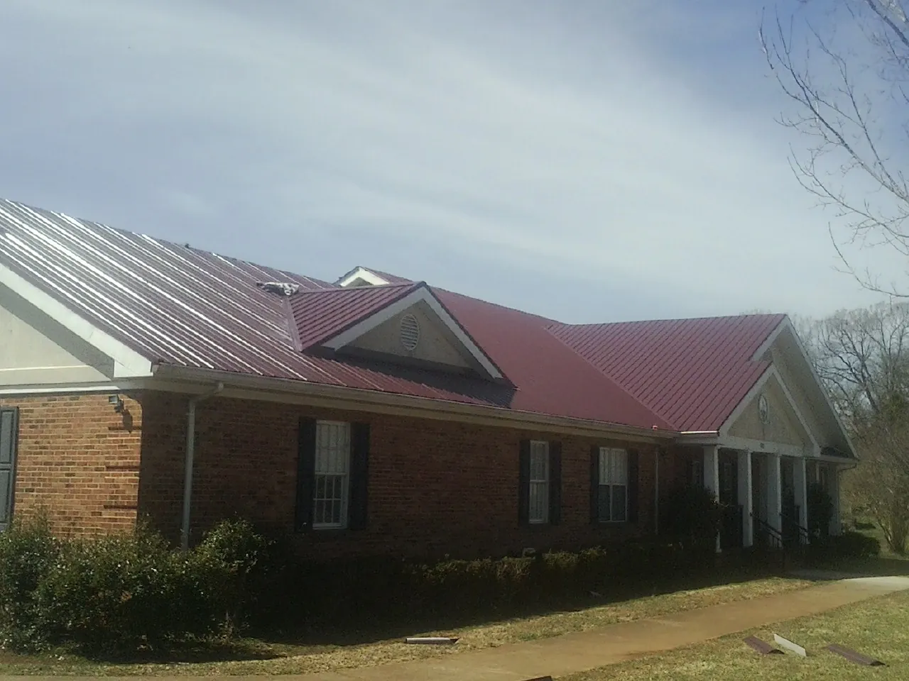 Red metal roof with gabled entries on a long brick building, from a Hail Damage Roof Repair job in Peru