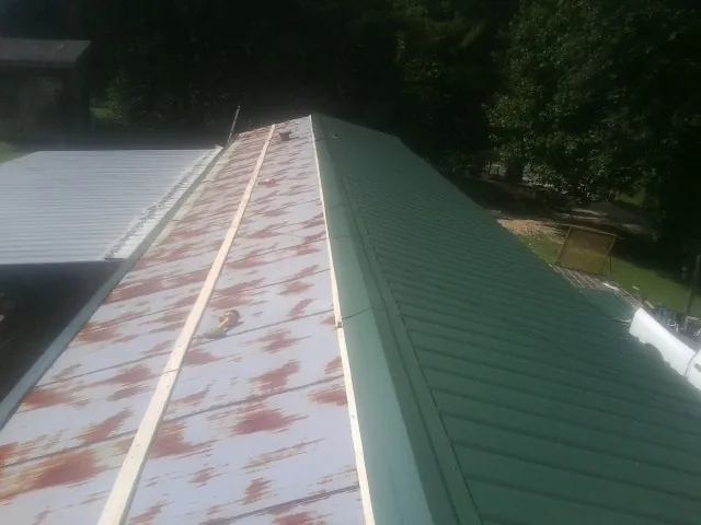 Old rusted panels beside newly installed green metal roofing — Wind Damage Roof Repair by Roofing Brothers in Peru